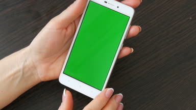 Eller güzel Fransız manikür ile yeşil ekran ile beyaz bir akıllı telefon alıyorum. Smartphone, Holding Smartphone bir şık siyah ahşap masa üstünde yeşil perde ile kullanma