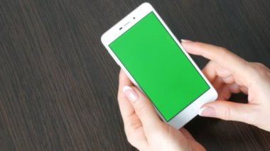 Eller güzel Fransız manikür ile yeşil ekran ile beyaz bir akıllı telefon alıyorum. Smartphone, Holding Smartphone bir şık siyah ahşap masa üstünde yeşil perde ile kullanma