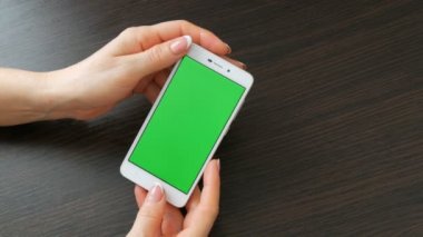 Eller güzel Fransız manikür ile yeşil ekran ile beyaz bir akıllı telefon alıyorum. Smartphone, Holding Smartphone bir şık siyah ahşap masa üstünde yeşil perde ile kullanma