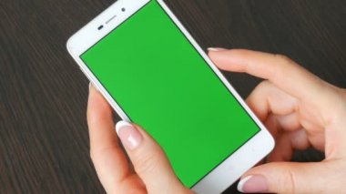 Eller güzel Fransız manikür ile yeşil ekran ile beyaz bir akıllı telefon alıyorum. Smartphone, Holding Smartphone bir şık siyah ahşap masa üstünde yeşil perde ile kullanma