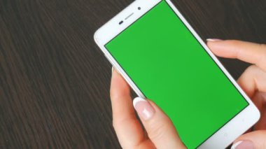 Eller güzel Fransız manikür ile yeşil ekran ile beyaz bir akıllı telefon alıyorum. Smartphone, Holding Smartphone bir şık siyah ahşap masa üstünde yeşil perde ile kullanma