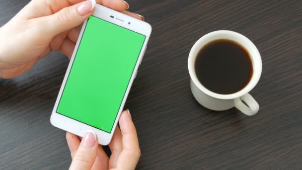 Ženské ruce s krásnou francouzskou manikúru si bílý smartphone s Green Screen poblíž bílý šálek kávy. Pomocí Smartphone, držení Smartphone s zelená obrazovka — Stock video