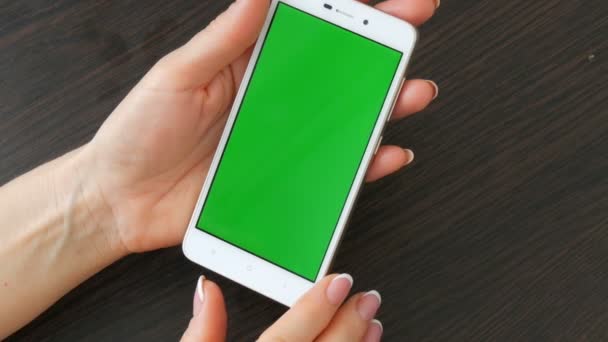 Женские руки с красивым французским маникюром возьмите белый смартфон с зеленым экраном. Использование смартфона, держа смартфон с зеленым экраном на стильном черном деревянном столе — стоковое видео