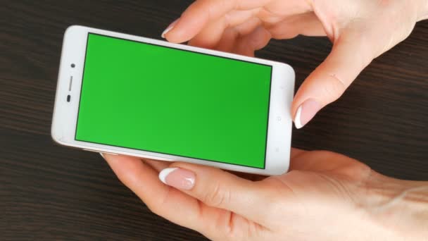 Женские руки с красивым французским маникюром возьмите белый смартфон с зеленым экраном. Использование смартфона, проведение смартфона с зеленым экраном — стоковое видео