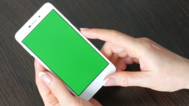 Eller güzel Fransız manikür ile yeşil ekran ile beyaz bir akıllı telefon alıyorum. Smartphone, Holding Smartphone bir şık siyah ahşap masa üstünde yeşil perde ile kullanma