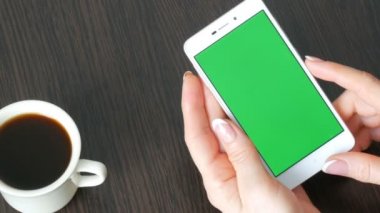 Eller güzel Fransız manikür ile beyaz bir akıllı telefon ile yeşil perde beyaz kahve götüreceğim. Smartphone, Holding Smartphone bir şık siyah ahşap masa üstünde yeşil perde ile kullanma