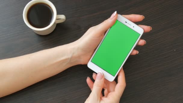 Жіночих рук з красивою французького манікюру взяти білий смартфон з зелений екран біля білого чашку кави. За допомогою смартфона, проведення смартфон з зелений екран на стильний чорний дерев'яний стіл — стокове відео