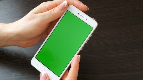 Női kezek gyönyörű francia manikűr vesz egy zöld képernyő fehér okostelefon. Használ Smartphone, gazdaság Smartphone-val egy elegáns fekete fából készült asztal Green Screen — Stock videók