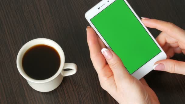Жіночих рук з красивою французького манікюру взяти білий смартфон з зелений екран біля білого чашку кави. За допомогою смартфона, проведення смартфон з зелений екран — стокове відео