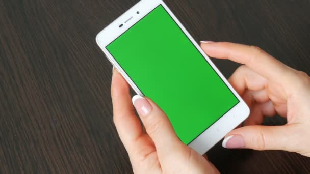 Las manos femeninas con hermosa manicura francesa toman un teléfono inteligente blanco con pantalla verde. Usando Smartphone, sosteniendo Smartphone con pantalla verde en una elegante mesa de madera negra — Vídeo de stock