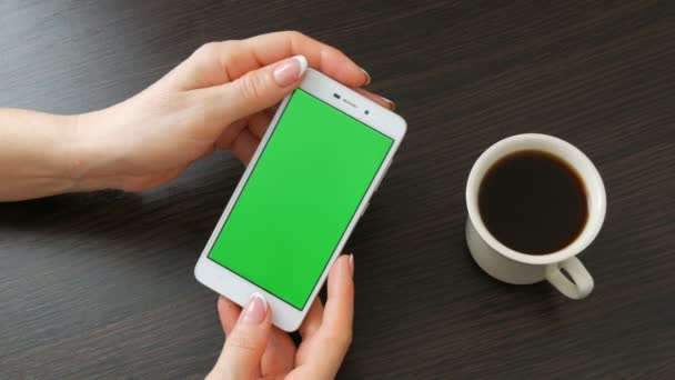 아름 다운 프랑스 매니큐어와 여성 손에 커피의 흰색 컵 근처 녹색 화면 흰색 스마트폰 걸릴. 스마트폰, 스마트폰 들고 세련 된 검은 나무의 테이블에 녹색 스크린을 사용 하 여 — 비디오