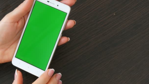 Les mains féminines avec une belle manucure française prennent un smartphone blanc avec écran vert. Utilisation de Smartphone, tenant Smartphone avec écran vert sur une table en bois noir élégant — Video