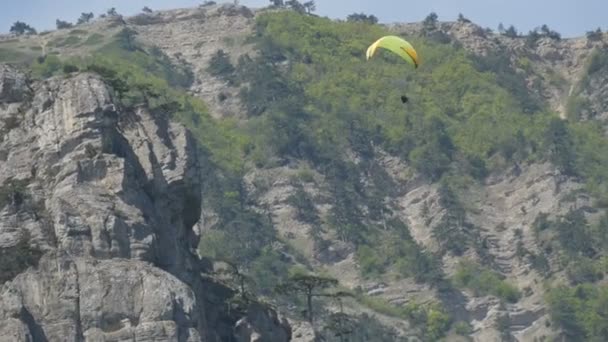 Parapente amarelo voa contra um fundo de montanhas verdes rochosas da Crimeia — Vídeo de Stock