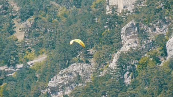 Gelber Gleitschirm fliegt vor dem Hintergrund grüner felsiger Krimberge — Stockvideo