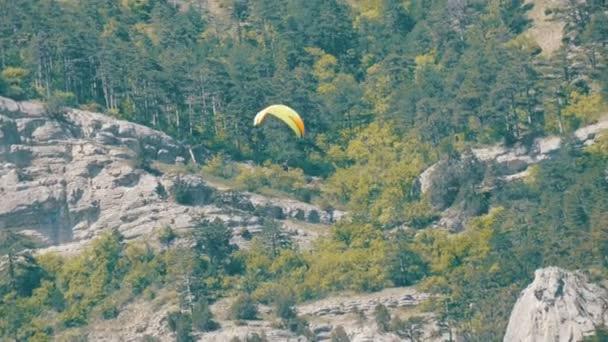 Желтый параплан летит на фоне зеленых скалистых гор Крыма — стоковое видео