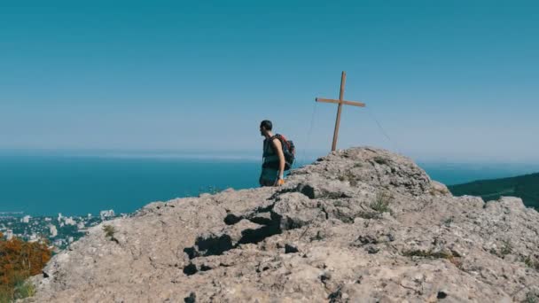 Traveler dengan ransel di punggungnya turun dari puncak gunung, dengan salib di puncak. Mencapai tujuan, motivasi untuk bangkit. . — Stok Video