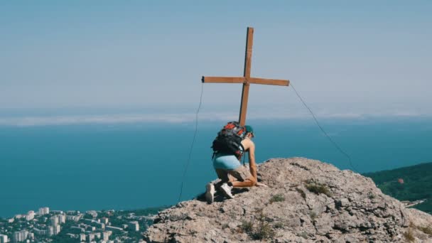 Viajante do sexo masculino com uma mochila nas costas atinge o topo da montanha, com uma cruz no pico. Alcançar o objetivo, motivação para subir . — Vídeo de Stock