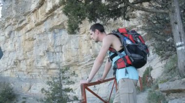 Sırtında kırmızı bir sırt çantası ile genç adam büyük bir kayanın yanında duruyor ve dağlara mesafe içine görünüyor