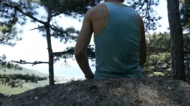 Genç bir adam bir yükseltilmiş platform üzerinde oturur ve güzel dağ manzarası mesafe, görünüm geri gelen görünüyor