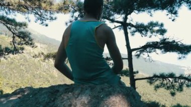 Genç bir adam bir yükseltilmiş platform üzerinde oturur ve güzel dağ manzarası mesafe, görünüm geri gelen görünüyor