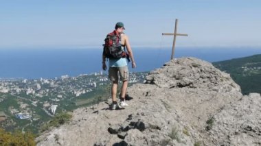 Sırtında bir sırt çantası ile erkek gezgin zirvesinde bir haç ile dağın zirvesine ulaşır. Başarı hedefi, motivasyon yükselmeye.