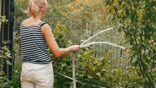 Frau gießt Pflanzen in ihrem Garten aus einem Schlauch — Stockvideo