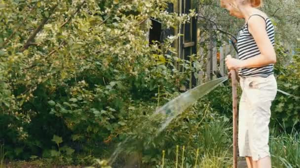 Женщина поливает растения в своем саду из шланга — стоковое видео