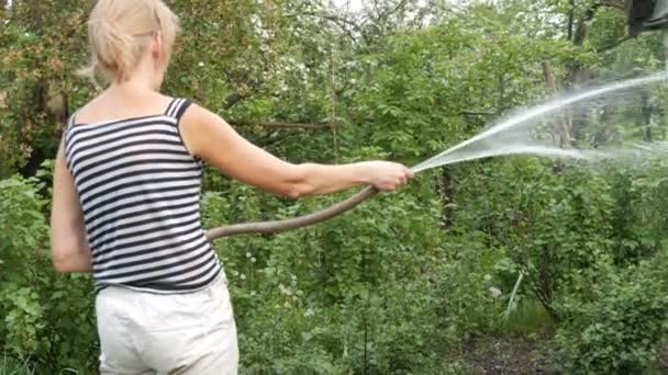 Mujer está regando plantas en su jardín de una manguera — Vídeos de Stock