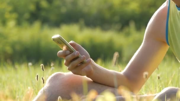 Jonge man kijkt naar de smartphone en iets worden afgedrukt op het groene gras tegen de achtergrond van een mooie zomerse natuur — Stockvideo