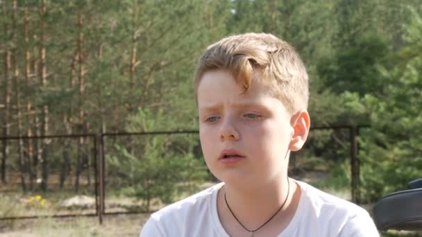 Jolie blonde aux yeux bleus un adolescent s'assoit dans un parc à côté de la bicyclette et parle en été. Portrait émotionnel d'un garçon 