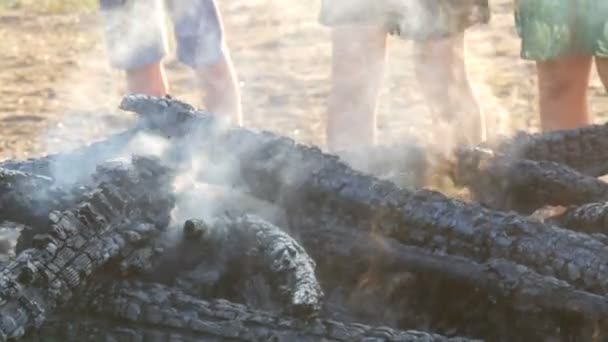 Brände till kolen, svart träd rök mot bakgrund av fötterna på personer — Stockvideo
