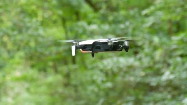 Un drone ou un quadrocopter de couleur blanche vole dans les airs sur fond de forêt verte. Technologies futures — Video