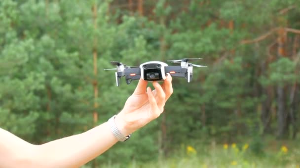 Una mano di uomo tiene un drone o un quadrocopter sullo sfondo di una foresta verde. Tecnologie future — Video Stock