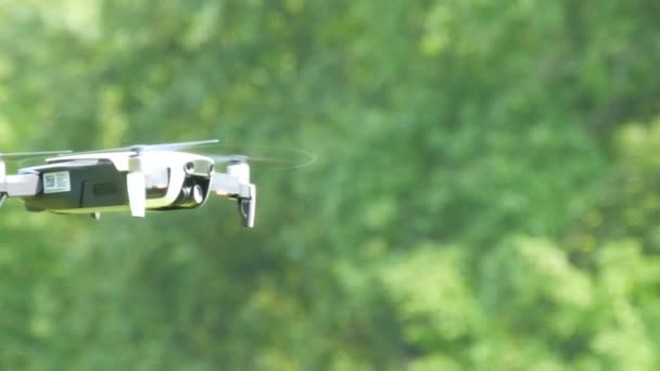En drone eller firedrokopter av hvit farge flyr i luften mot bakgrunnen av en grønn skog. Framtidige teknologier – stockvideo