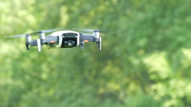 Un drone ou un quadrocopter de couleur blanche vole dans les airs sur fond de forêt verte. Technologies futures — Video