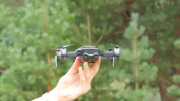 Mans hånd holder en drone eller et firkløverfly og slipper ut mot bakgrunnen av en grønn skog. Framtidige teknologier – stockvideo