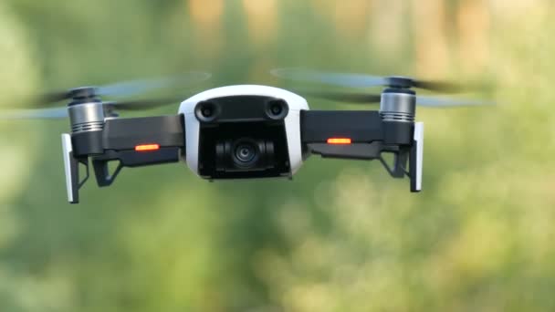 Белый или квадровертолетный дрон в полете на фоне зеленой природы, вид вблизи — стоковое видео