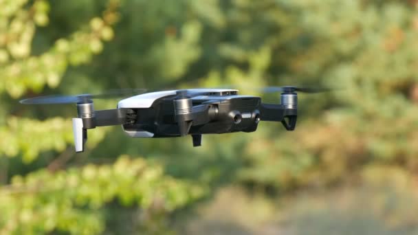 White or quadrocopter drone in flight against background of green nature, close up view — Stock Video