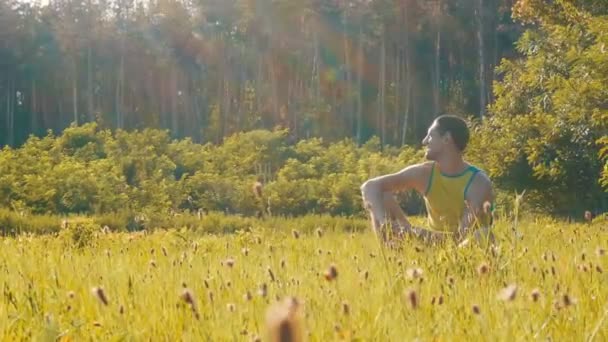 Wesoły, młody człowiek siedzi na zielonej trawie w lato i uśmiecha się — Wideo stockowe