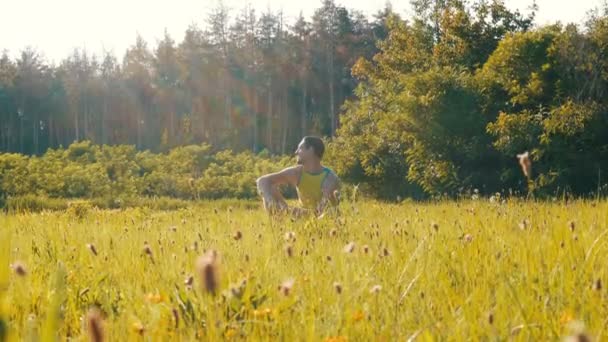 Веселий молодий чоловік сидить на зеленій траві влітку і посміхається — стокове відео