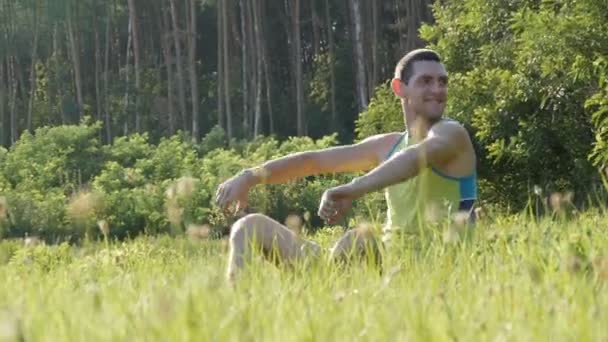 Joven sentado en la naturaleza en la hierba feliz disfrutando de la vida y sonriendo — Vídeo de stock