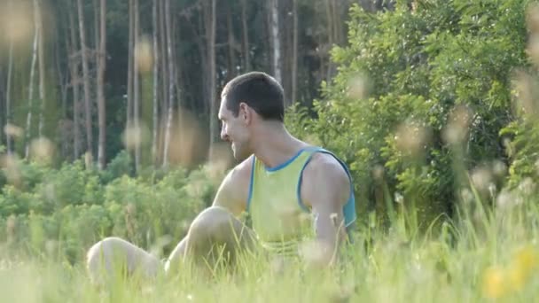 Junger Mann sitzt glücklich im Gras und genießt das Leben und lächelt — Stockvideo