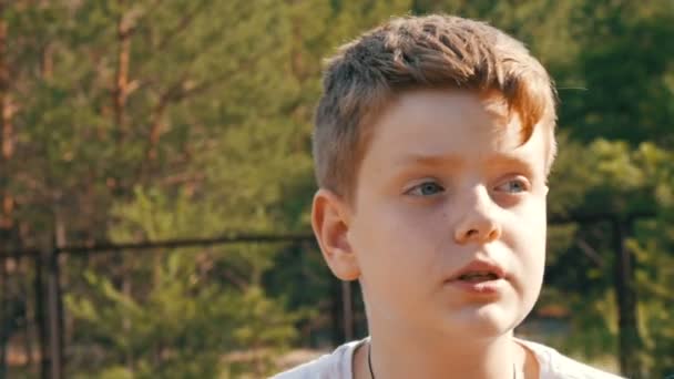 Jolie blonde aux yeux bleus un adolescent s'assoit et sourit dans un parc à côté de la bicyclette et parle en été. Portrait émotionnel d'un garçon 