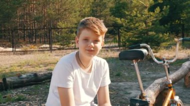 Mavi gözlü tatlı bir sarışın bir genç çocuk oturur ve bisiklet ve görüşmeler yanındaki bir parkta yaz aylarında gülümse. Bir çocuğun duygusal portre