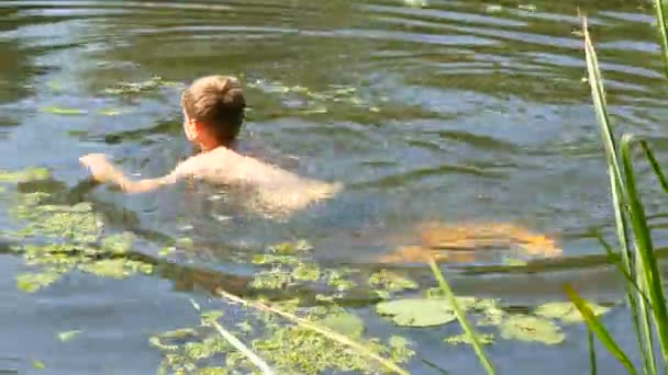 Menino adolescente está tomando banho em um rio selvagem no verão. Bing Ervas daninhas no rio em condições naturais — Vídeo de Stock