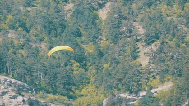 Parapente amarelo voa contra um fundo de montanhas verdes rochosas da Crimeia — Vídeo de Stock