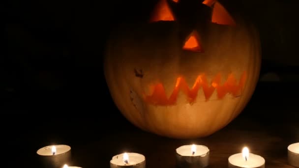 Terrible calabaza de Halloween rodeada de muchas velas en la oscuridad — Vídeos de Stock