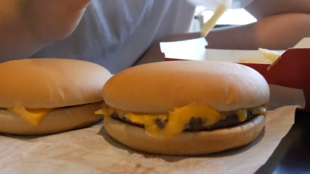 Adolescente está comiendo papas fritas fritas con cebolla y queso. La mano perfora un tenedor de plástico con comida malsana o comida rápida junto a hamburguesas grandes con queso — Vídeos de Stock