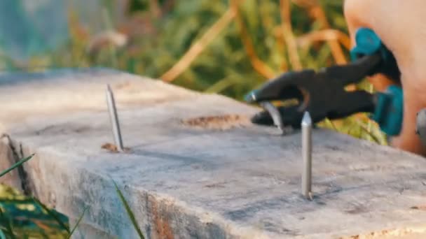 Человек сгибает железные гвозди с плоскогубцами на старой доске — стоковое видео