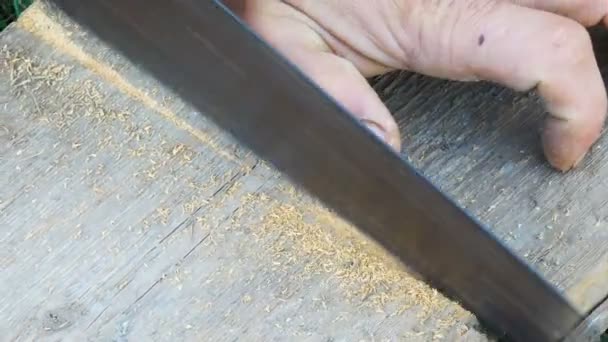 Чоловік розпилює дерев'яну дошку з ручною пилкою — стокове відео